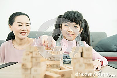 Asian mother and daughter playing wood block tower stacking game in cozy modern home. Ethnic babysitter engaging little girl in Stock Photo