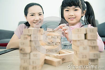 Asian mother and daughter playing wood block tower stacking game in cozy modern home. Ethnic babysitter engaging little girl in Stock Photo