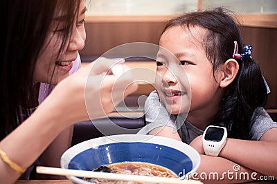 Asian mother helped blow the food to cool for the daughter to eat noodle Stock Photo