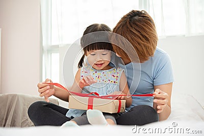 Child daughter unwrapping gift box with her mom. Stock Photo