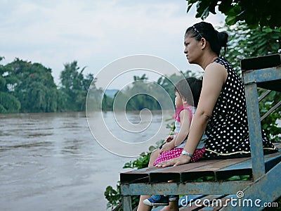 Asian mother and her little daughter by her side looking at murky muddy river after rainfall Stock Photo