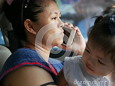 Asian mother uncomfortably making a phone call while dealing with her daughter in a driving car Stock Photo