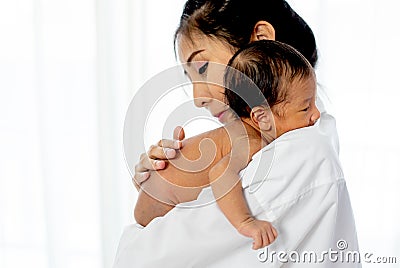 Asian mother with white shirt place upon the shoulder of little newborn baby after give milk and the baby look sleepy Stock Photo