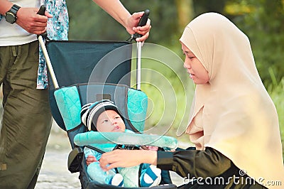 Asian muslim hijabi mother and father walk through the park with son in stroller Stock Photo