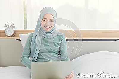 Asian Muslim Islamic woman with hijab happy enjoy online remote work at home with her laptop on the bed Stock Photo