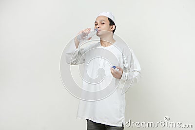 asian muslim man drinking from palstic water bottle on isolated background Stock Photo
