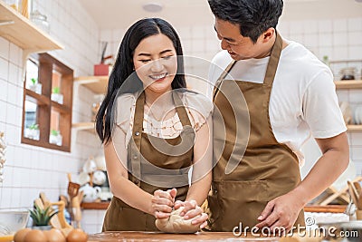 Asian new marriage couple stay home, spend time together in kitchen. Romance Young attractive husband and wife enjoy kneaded yeast Stock Photo