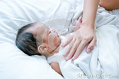 Asian newborn baby is sleeping on white bed with mother hand put on her chest to take care and make her feel safe Stock Photo