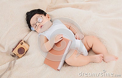 Asian Newborn baby wearing glasses with favorite book on beige blanket , 3 month-old infant lying in bed with relax. Adorable baby Stock Photo