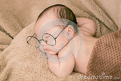 Asian Newborn baby wearing glasses and sleep on brown bed at home, 0-1month-old infant lying in blanket with relax. Adorable baby Stock Photo