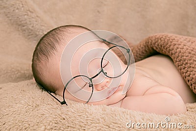 Asian Newborn baby wearing glasses and sleep on brown bed at home, 0-1month-old infant lying in blanket with relax. Adorable baby Stock Photo