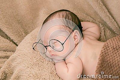 Asian Newborn baby wearing glasses and sleep on brown bed at home, 0-1month-old infant lying in blanket with relax. Adorable baby Stock Photo