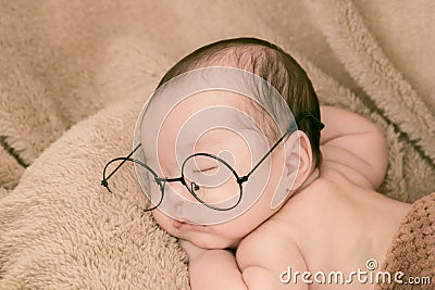 Asian Newborn baby wearing glasses and sleep on brown bed at home, 0-1month-old infant lying in blanket with relax. Adorable baby Stock Photo