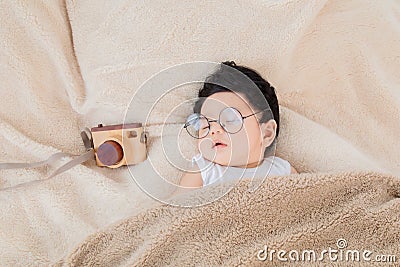 Asian Newborn baby wearing glasses sleeping with beige blanket next to toy camera with safe and comfortable. Adorable baby resting Stock Photo