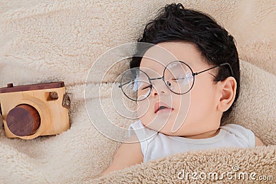 Asian Newborn baby wearing glasses sleeping with beige blanket next to toy camera with safe and comfortable. Adorable baby resting Stock Photo