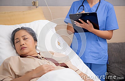 Asian nurse check saline and check patient elderly while asleep on bed at hospital ward, doctor diagnostic senior woman. Stock Photo