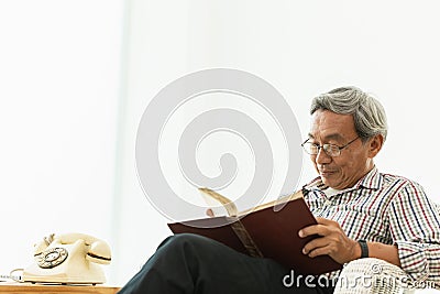 Asian Old man glasses professor sitting on the chair reading textbook Stock Photo