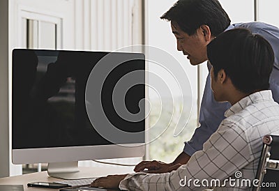 Asian old senior male father stand and young handsome teen son sit use index finger pointing blank empty black computer monitor Stock Photo