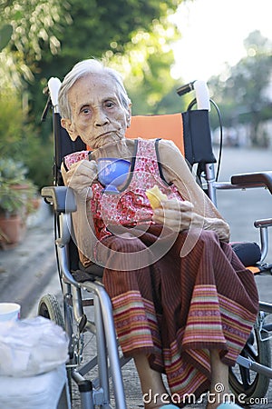 asian old woman sitting on whell chair and drinking warm beverage Stock Photo