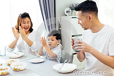 Asian parents clapping hands and giving compliment as their child does good job while having meal together at home. Stock Photo