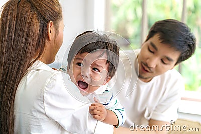 Asian Parents with mother and father trying to calm down crying infant son in living room at home Stock Photo