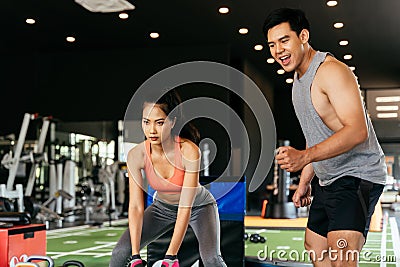 Asian personal trainer coaching a bodybuilding woman to perform crossfit battle ropes exercise in the fitness gym Stock Photo