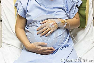 Asian Pregnant Woman patient is on drip receiving a saline solution on bed VIP room at hospital. Stock Photo
