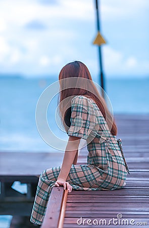 Asian pretty gilr wearing dress so alone feeling with walking and sit on walk way to to sea on evening Stock Photo