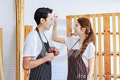 Asian professional female carpenter worker staff in apron smiling taking care of male lover couple using tissue paper wiping sweat Stock Photo