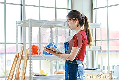 Asian professional female labor worker wears safety goggles and apron standing holding paper clipboard writing note checking stock Stock Photo