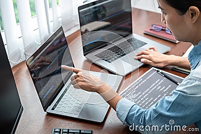 Asian programmer woman pointing and looking on multiple laptop screen to writing code and database Stock Photo