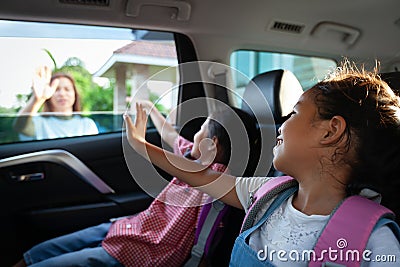 Asian pupil girl with backpack and her sister sitting in the car and waving goodbye to her mother Stock Photo