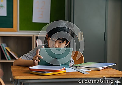 Asian school boy using digital device in school classroom, digital native, technology, learning, touchscreen. Male Stock Photo