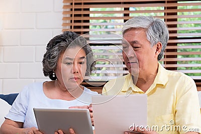 Asian senior couple calculate retirement financial use tablet searching document sitting on sofa at home,senior learn to use Stock Photo