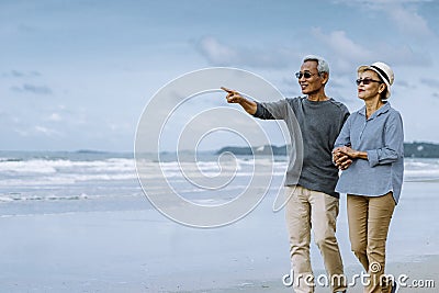 Asian senior couple or elderly people walking and siting at the beach Stock Photo