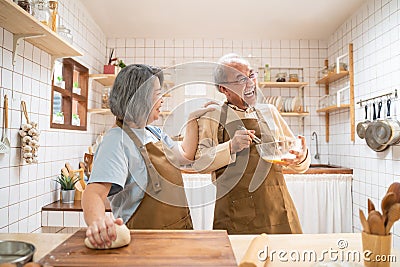 Asian senior couple standing in the kitchen at home, feeling happy and enjoy retirement life. Husband enjoy stirring eggs, wife Stock Photo