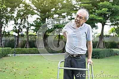 Asian Senior disabled man walking slowly with walker or cane at park. Older elderly mature handicapped patient male feeling Stock Photo