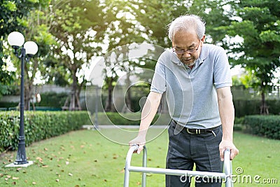 Asian Senior elderly disabled man patient walking slowly with walker or cane at green park. Older mature handicapped male feeling Stock Photo