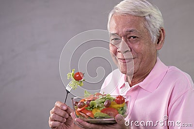 Asian senior man in joyful postures with hand holding salad bowl Stock Photo