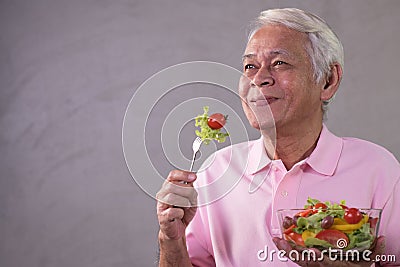 Asian senior man in joyful postures with hand holding salad bowl Stock Photo