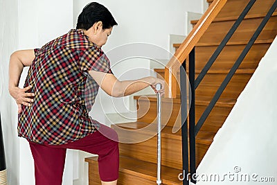 Asian senior older woman suffering from low-back lumbar pain while walking on stair at home Stock Photo