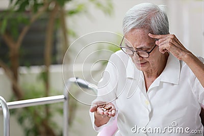 Asian senior patient with Alzheimer`s disease or dementia,look at the pills capsules on her palm,trying to think,confused,old Stock Photo