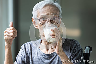 Asian senior woman drinking fresh milk from the glass,old elderly holding glass of milk,showing thumb up while drinking and Stock Photo