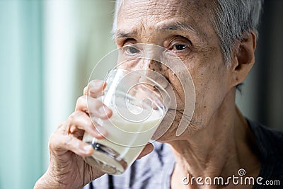 Asian senior woman drinking warm fresh milk from glass in the morning at home,old elderly eat foods that are beneficial to the Stock Photo