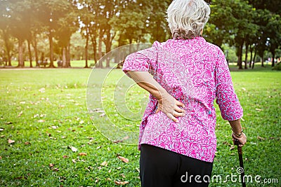 Asian senior woman hands touching back pain while walking in nature in summer,female patient having backache,muscle,hip pain in Stock Photo