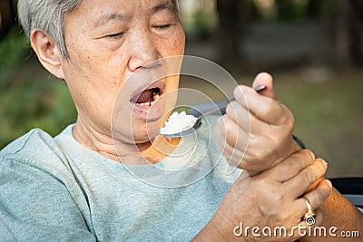 Asian senior woman holding spoon and hands tremor while eating rice,cause of hands shaking include parkinson`s disease,stroke, Stock Photo