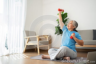 Asian senior woman lifting dumbbell for exercise and workout at home. Active mature woman doing stretching exercise in living room Stock Photo