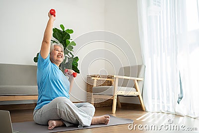 Asian senior woman lifting dumbbell for exercise and workout at home. Active mature woman doing stretching exercise in living room Stock Photo