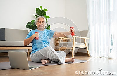 Asian senior woman lifting dumbbell for exercise and workout at home. Active mature woman doing stretching exercise in living room Stock Photo