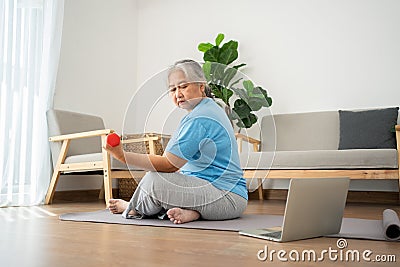 Asian senior woman lifting dumbbell for exercise and workout at home. Active mature woman doing stretching exercise in living room Stock Photo